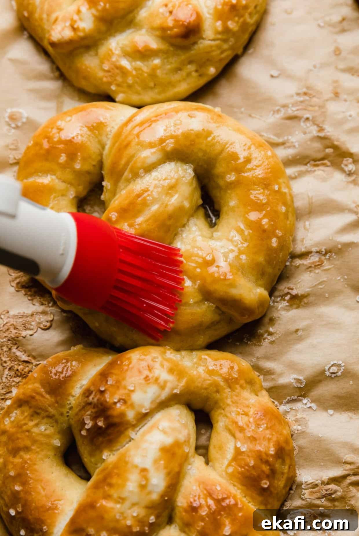 Perfect Homemade Soft Pretzels 9 A red pastry brush expertly spreading melted butter over a warm, golden-baked pretzel, fresh from the oven, creating a luxurious sheen.