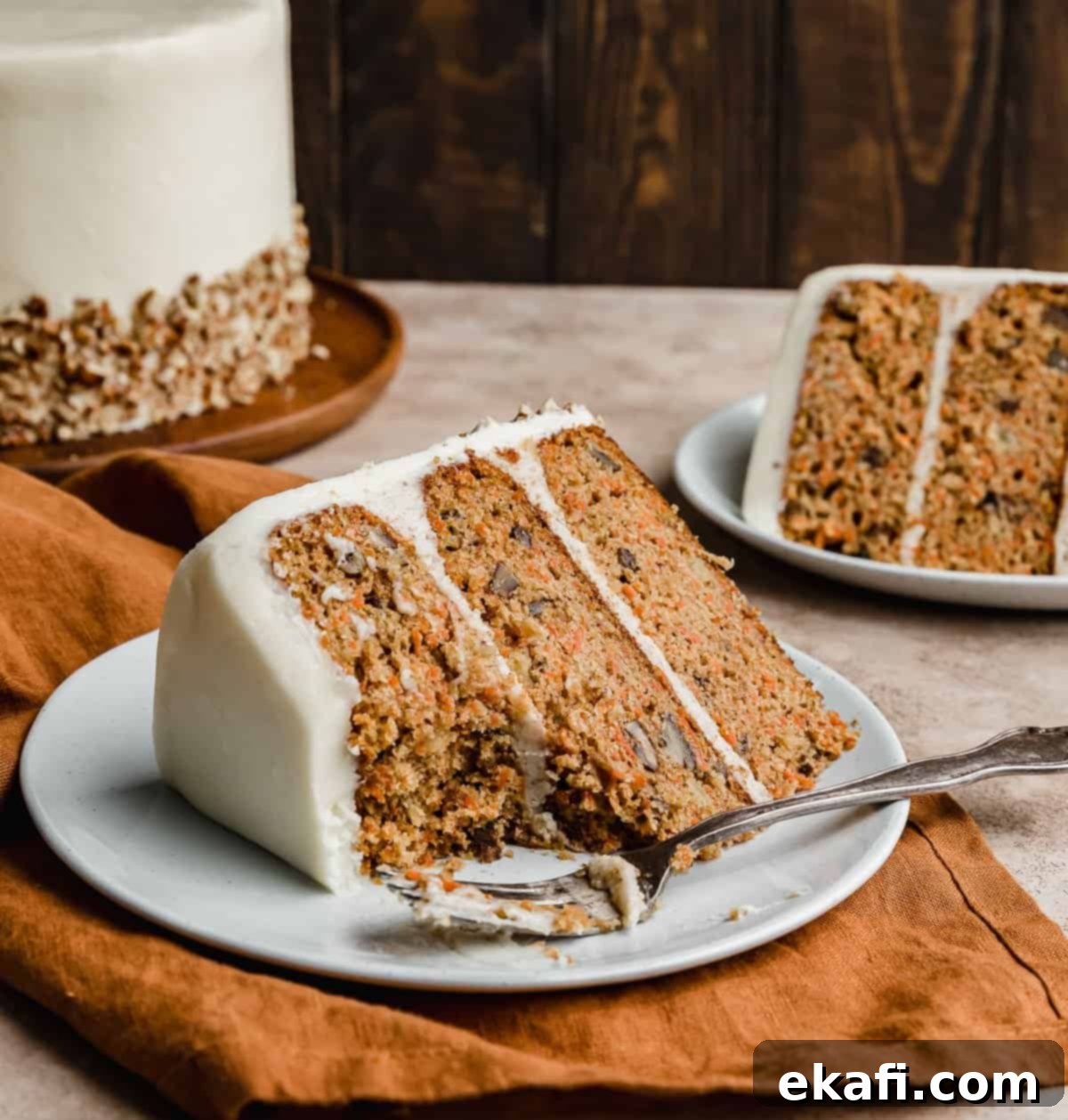 Tropical Pecan Carrot Cake 11 A delectable slice of a three-layered carrot cake, artfully arranged on a clean white plate, set against a cozy burnt orange linen napkin.