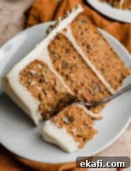 Tropical Pecan Carrot Cake 12 A slice of moist carrot cake with crushed pineapple and pecans, beautifully frosted and presented on a white plate, with a fork gently cutting into the cake to reveal its tender layers.