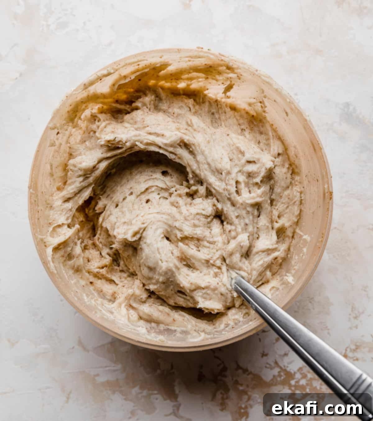 Tropical Pecan Carrot Cake 5 A beige-colored bowl filled with luscious toasted pecan buttercream, ready to be spread, against a clean white background.