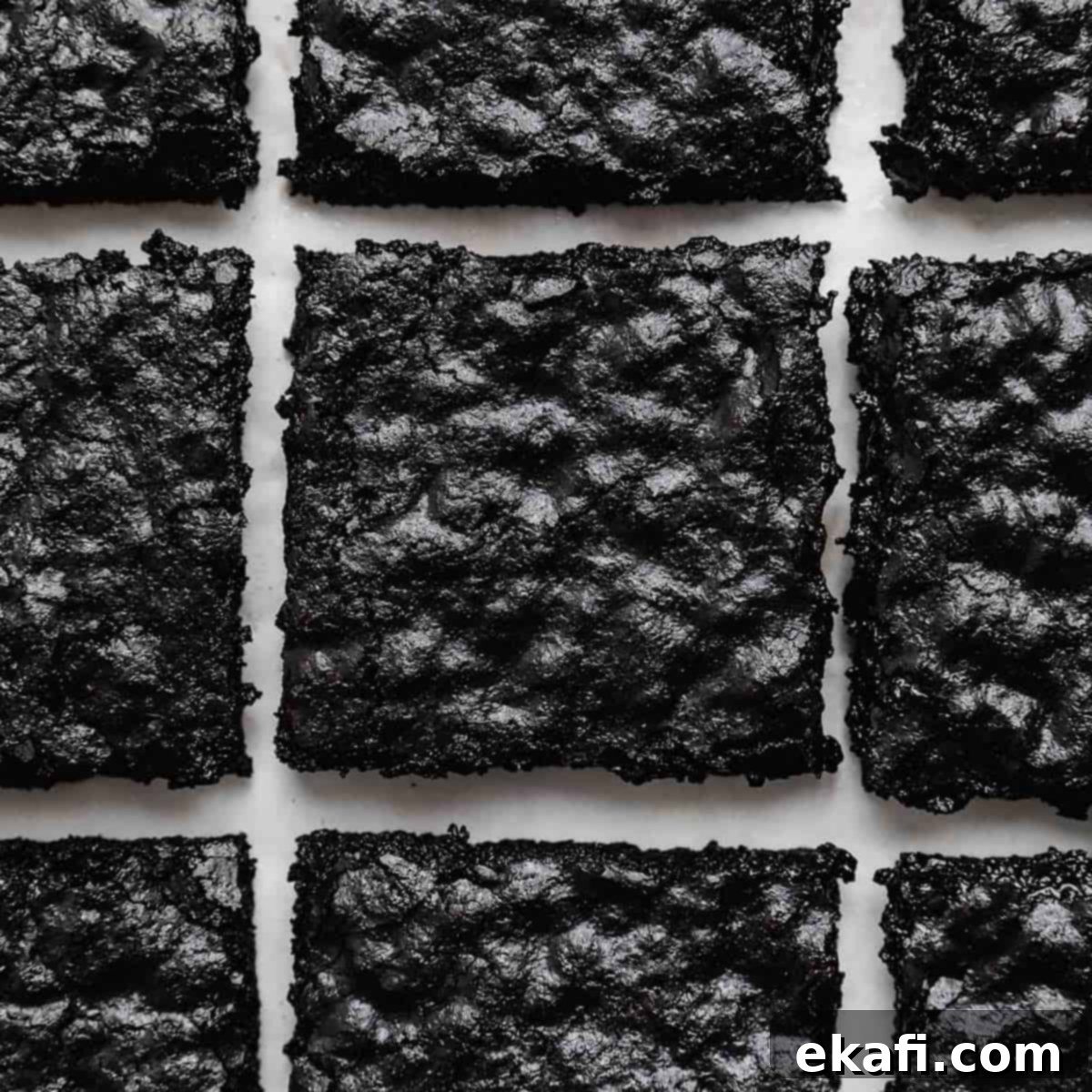 Deep & Dark Black Cocoa Delights 9 Crackly top Black Cocoa Brownies cut into squares on a white background.