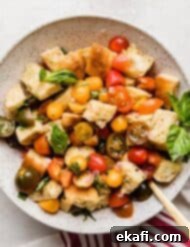 Rustic Tuscan Panzanella 10 A bowl of Panzanella Toscana topped with fresh basil on a white background.