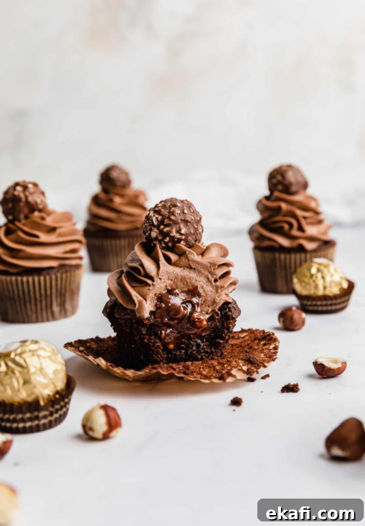 Decadent Ferrero Rocher Cupcakes 2 A Ferrero Rocher Cupcake with a bite taken out of it showing the inside of the cupcake filled with Nutella.