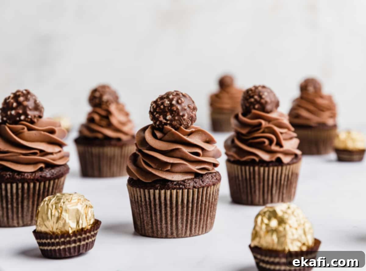 Decadent Ferrero Rocher Cupcakes 11 Several Ferrero Rocher Cupcakes topped with a swirl of chocolate frosting and a Ferrero Rocher candy on top, against a white background.