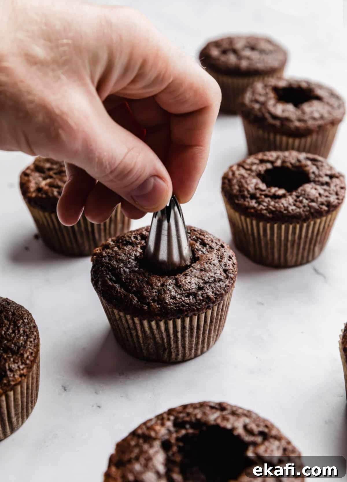 Decadent Ferrero Rocher Cupcakes 7 A hand using a piping tip to remove the core of a chocolate cupcake.