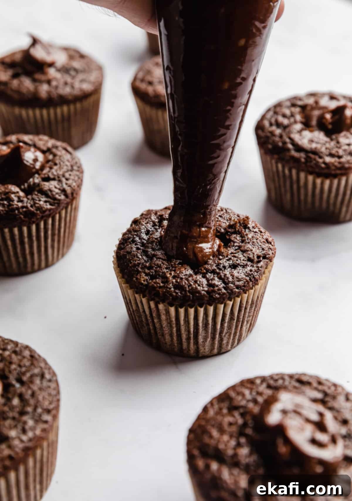 Decadent Ferrero Rocher Cupcakes 9 A piping bag filled with Nutella that's being dispensed into the center of a chocolate cupcake.