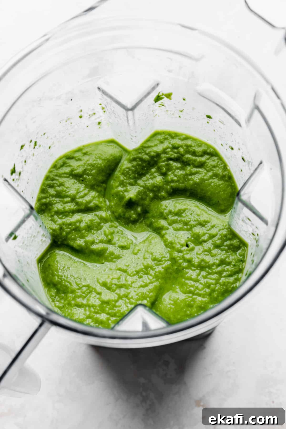 Σμούθι Ανανά Σπανάκι 5 Ένα παχύ πράσινο smoothie σε μπλέντερ, σε λευκό φόντο.