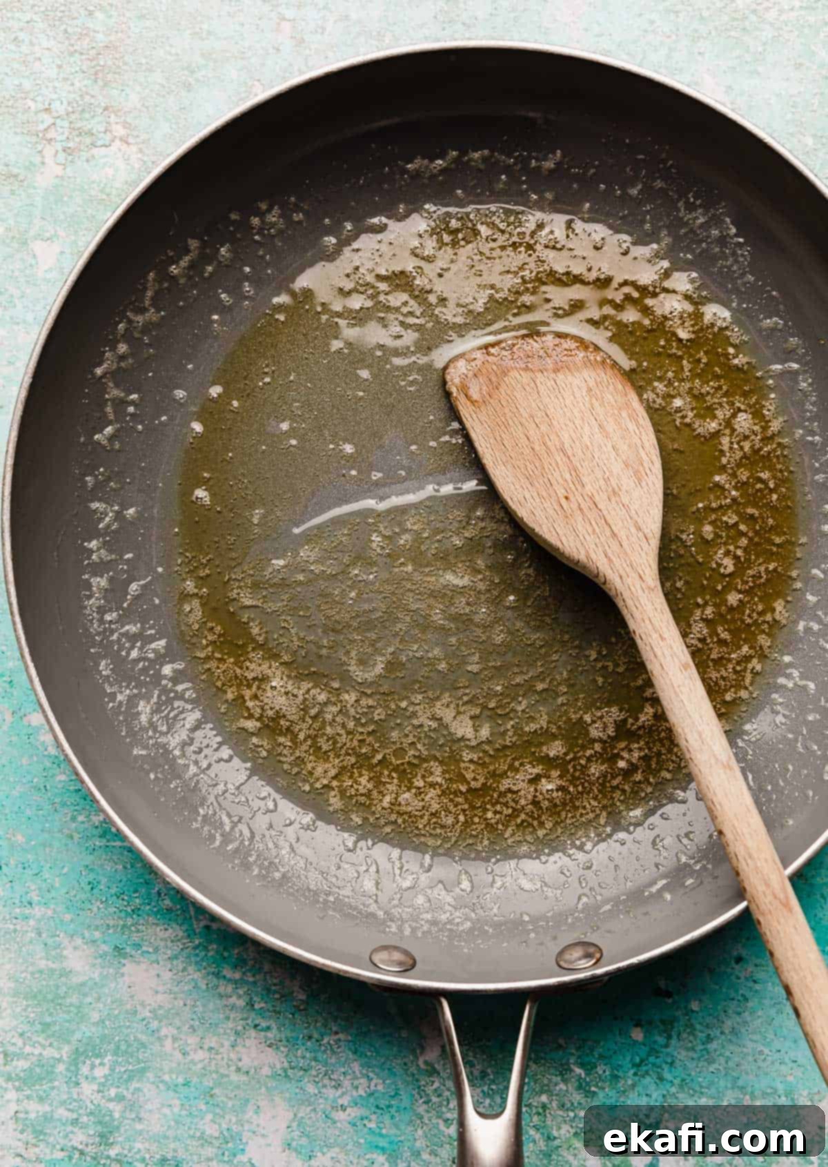 Golden Honey Butter Skillet Corn 4 Melted butter and honey in a gray skillet on a turquoise blue background.