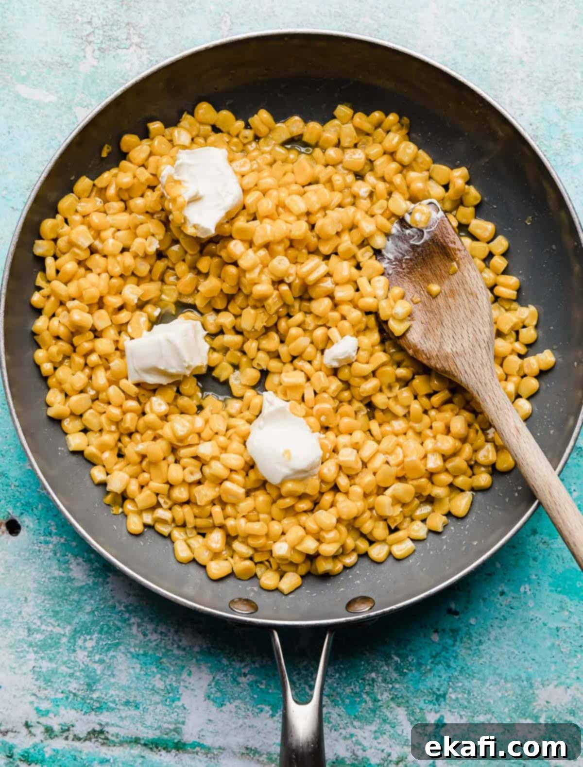 Golden Honey Butter Skillet Corn 6 Overhead photo of a grey skillet filled with corn kernels and three small squares of white cream cheese.