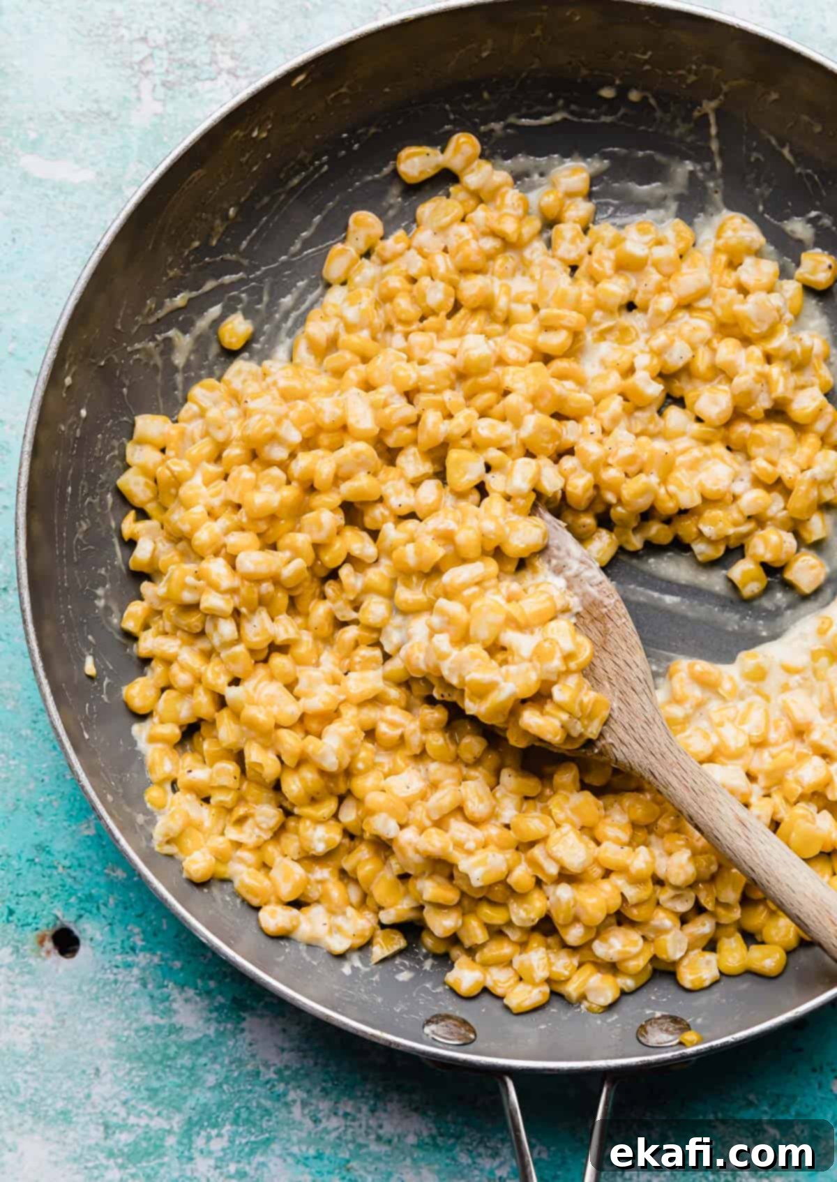 Golden Honey Butter Skillet Corn 7 Close up photo of Honey Butter Skillet Corn in a grey skillet with a wooden spoon scooping up some of the corn.