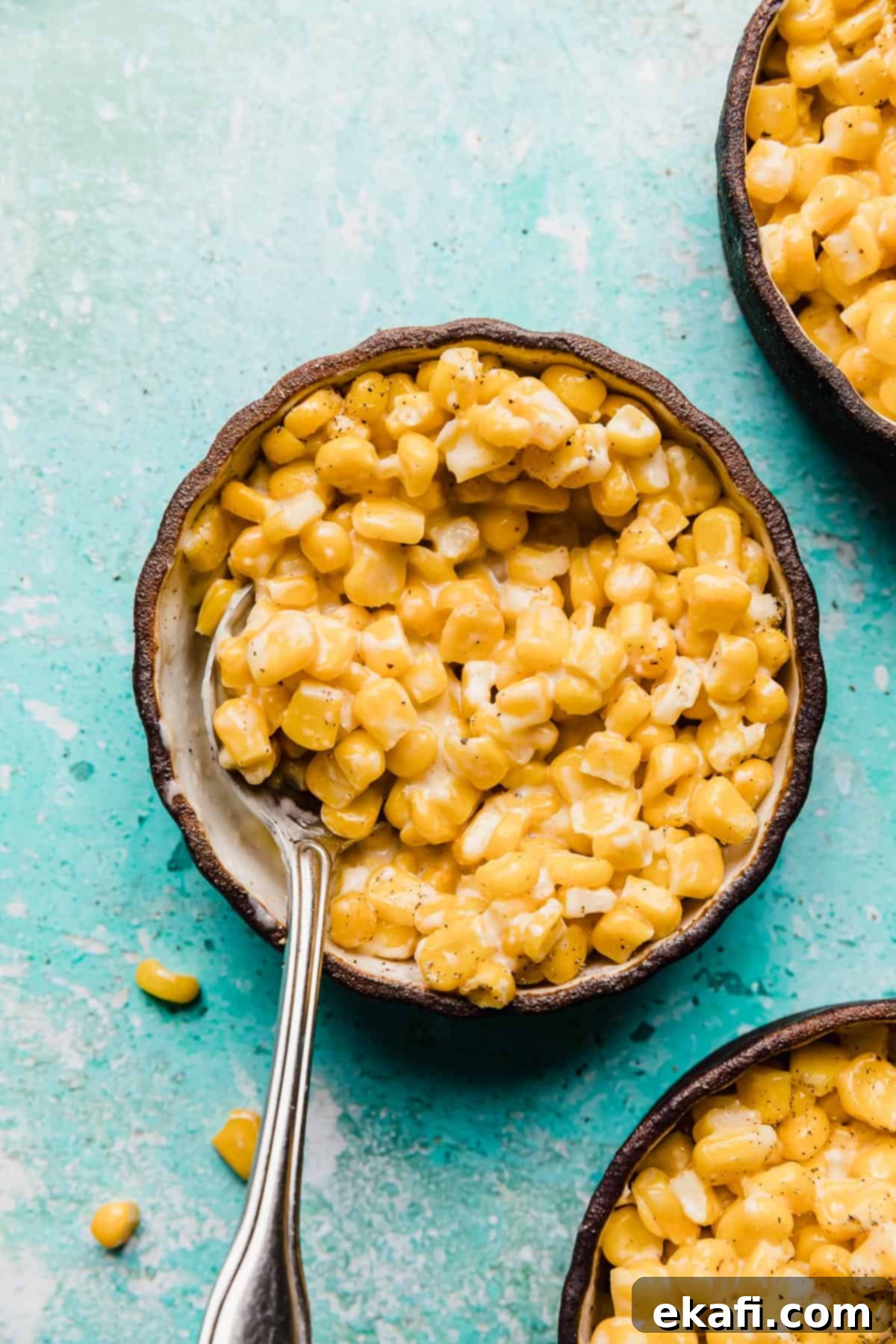 Golden Honey Butter Skillet Corn 8 A black bowl with Honey Butter Skillet Corn and a spoon in it, against a turquoise blue background.