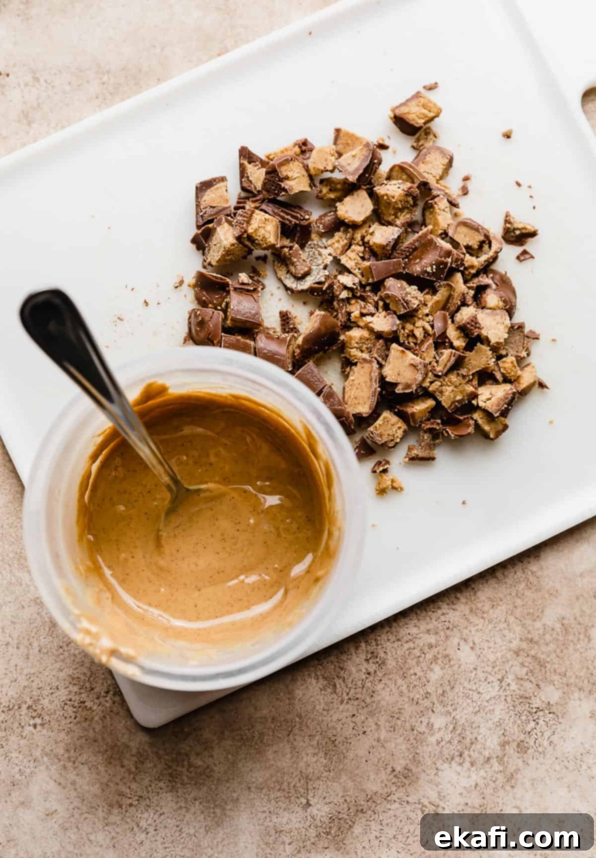 Decadent Peanut Butter Cup Cookies 3 Melted peanut butter in a clear bowl with chopped Reese's peanut butter cups to the right of the bowl.