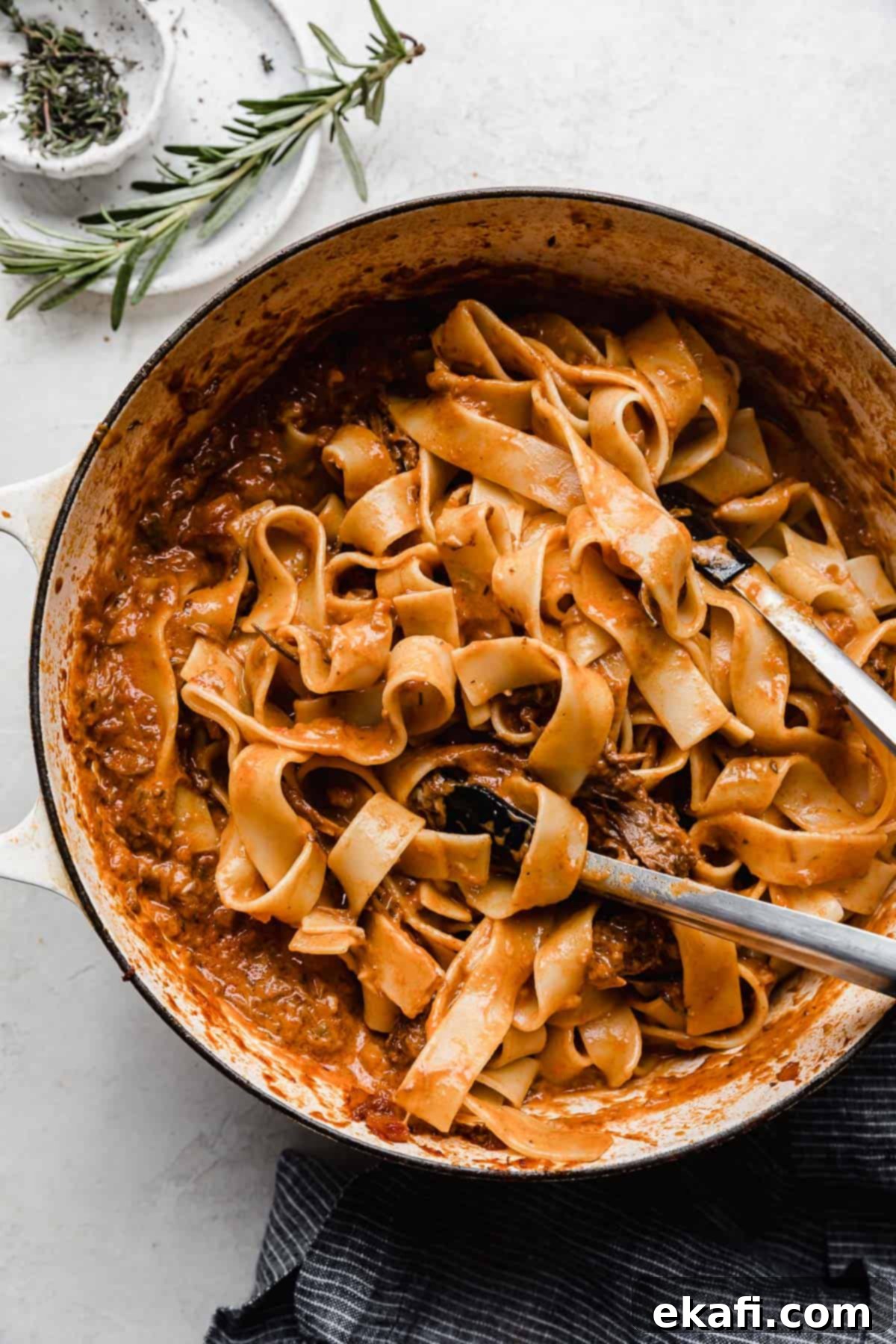 Hearty Shredded Beef Ragu 15 Kitchen tongs tossing Beef Ragu and pappardelle noodles in a white pot.