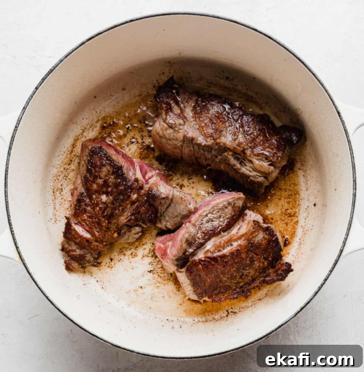 Hearty Shredded Beef Ragu 5 Three seared beef chuck roasts in a white pot.