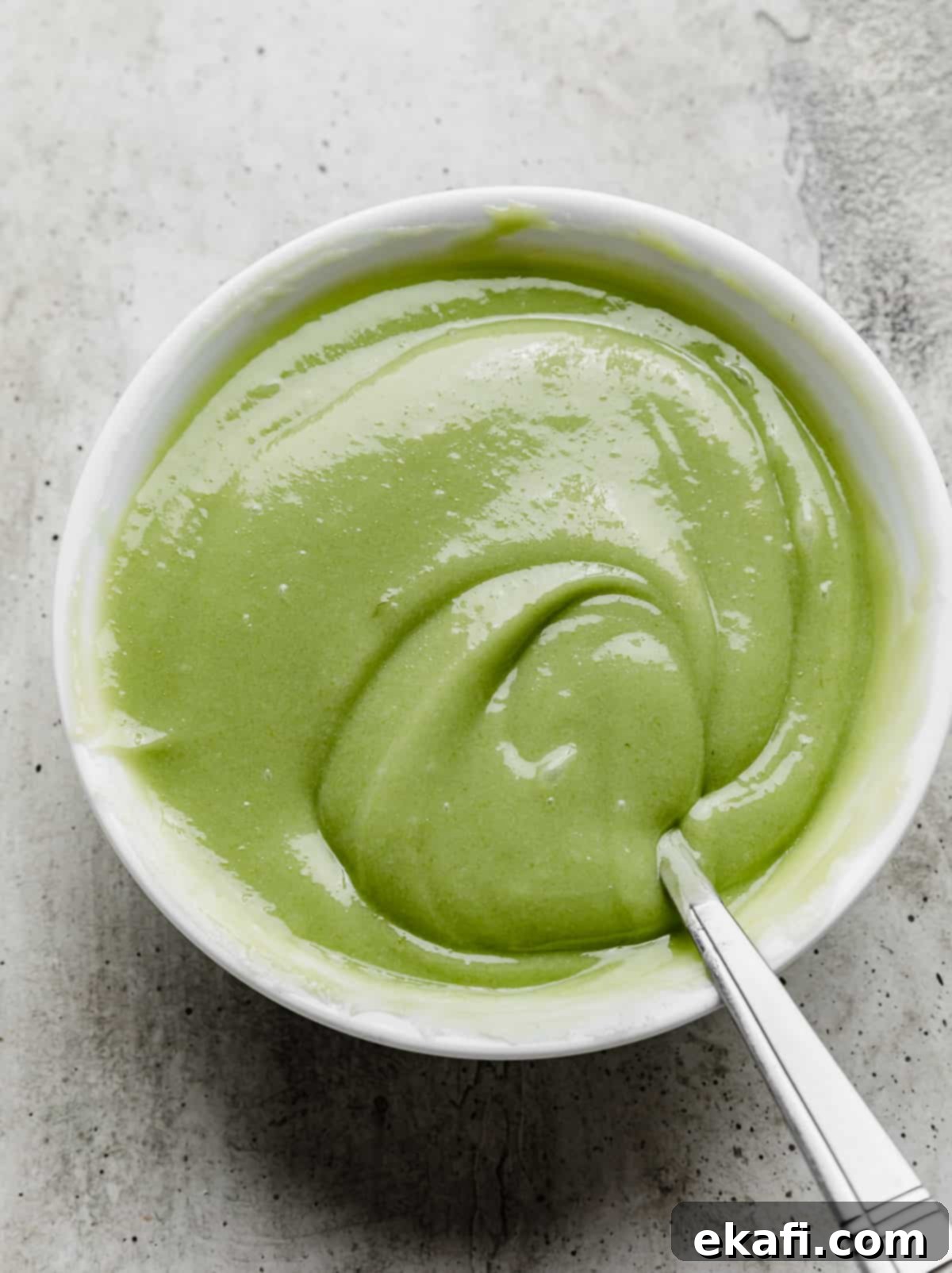 Key Lime Dream Cake 5 A lime green colored key lime curd in a white bowl on a grey textured background.