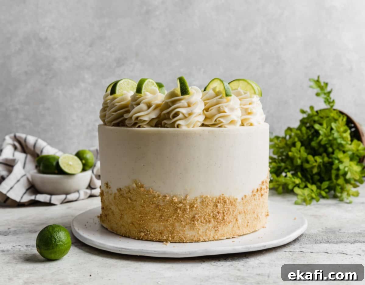 Key Lime Dream Cake 7 A Key Lime Cake topped with frosting swirls and lime slices against a light grey background.