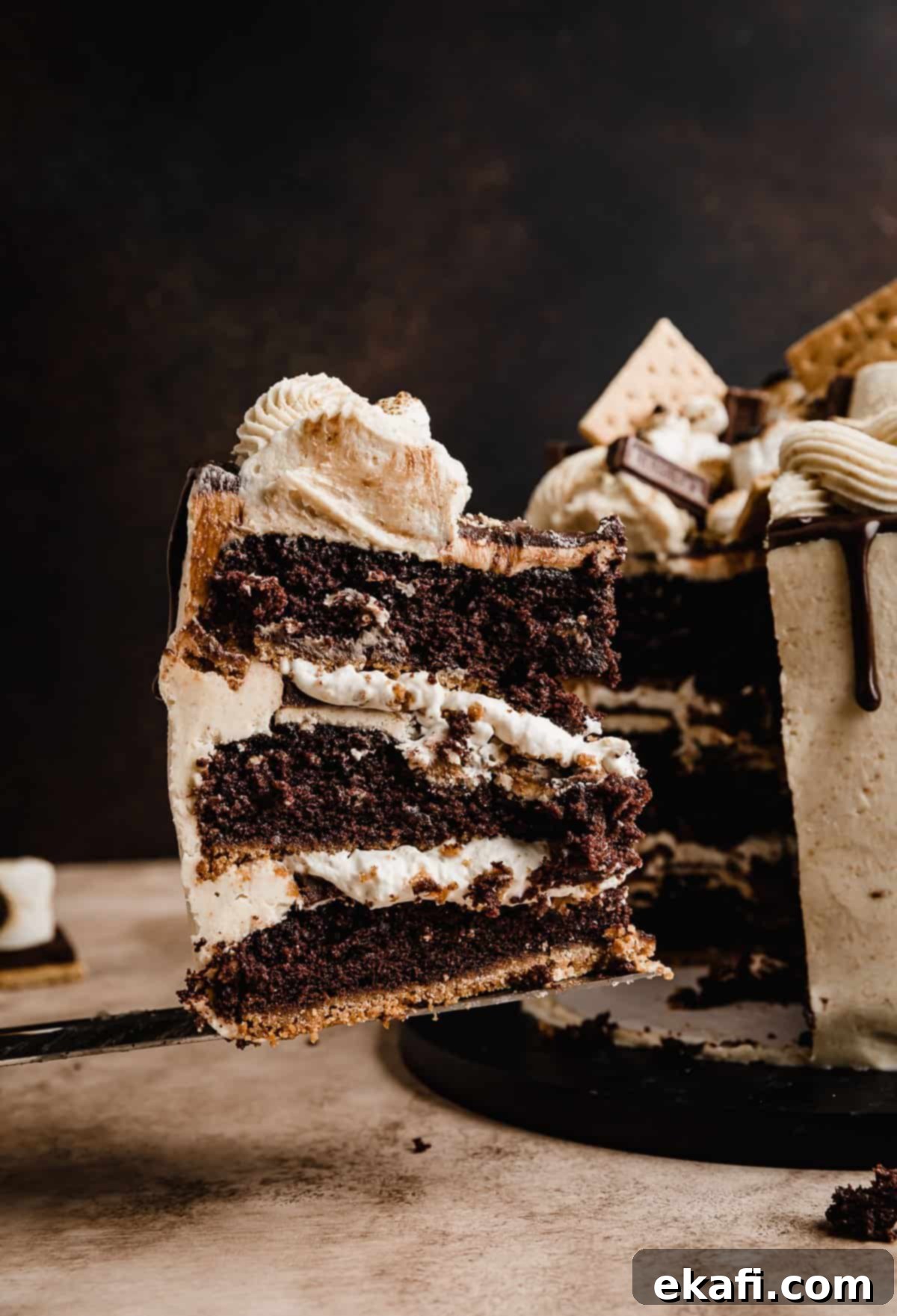 S'mores Cake 12 A slice of a S'mores three layer Cake balancing on a serving knife, in front of a brown background.