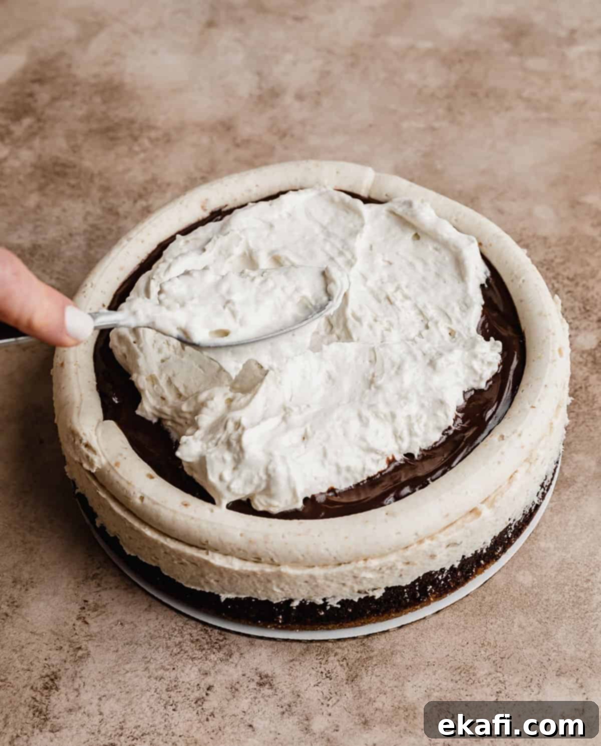 S'mores Cake 9 A fluffy marshmallow whipped cream being spread overtop a frosted S'mores Cake layer.