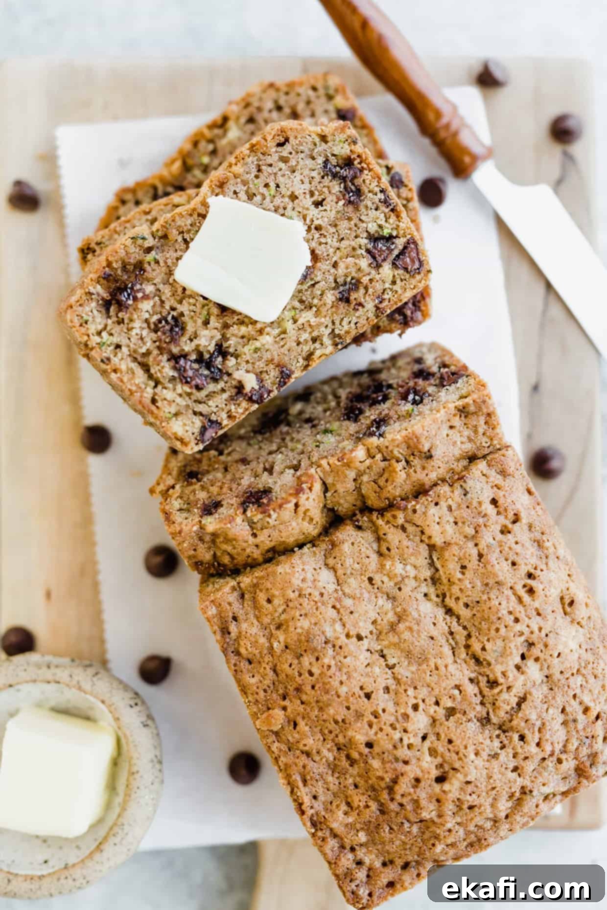 Decadent Chocolate Chip Zucchini Loaf 12 Overhead view of several slices of chocolate chip zucchini bread, with one slice featuring a square of butter.