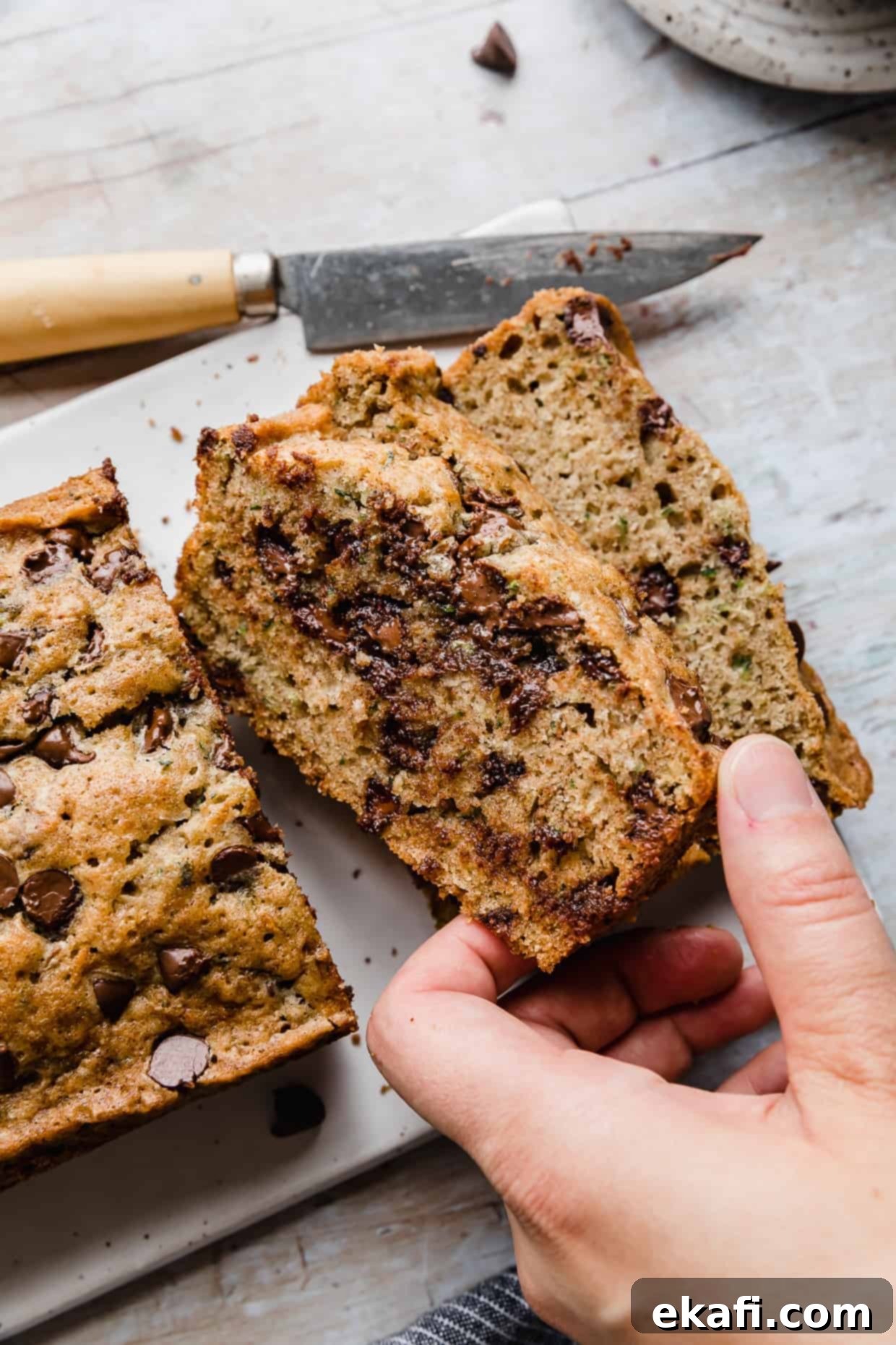 Decadent Chocolate Chip Zucchini Loaf 13 A hand reaching for a delicious slice of chocolate chip zucchini bread, inviting you to take a bite.