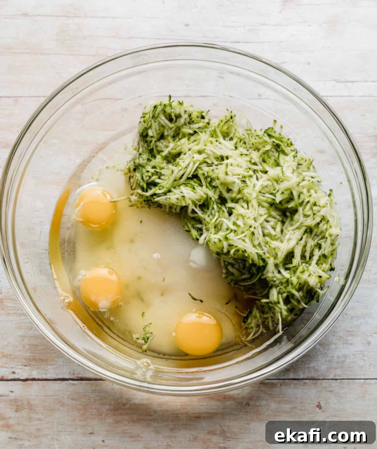 Decadent Chocolate Chip Zucchini Loaf 6 Shredded zucchini, eggs, sugar, and vanilla extract harmoniously mixed in a large glass bowl.