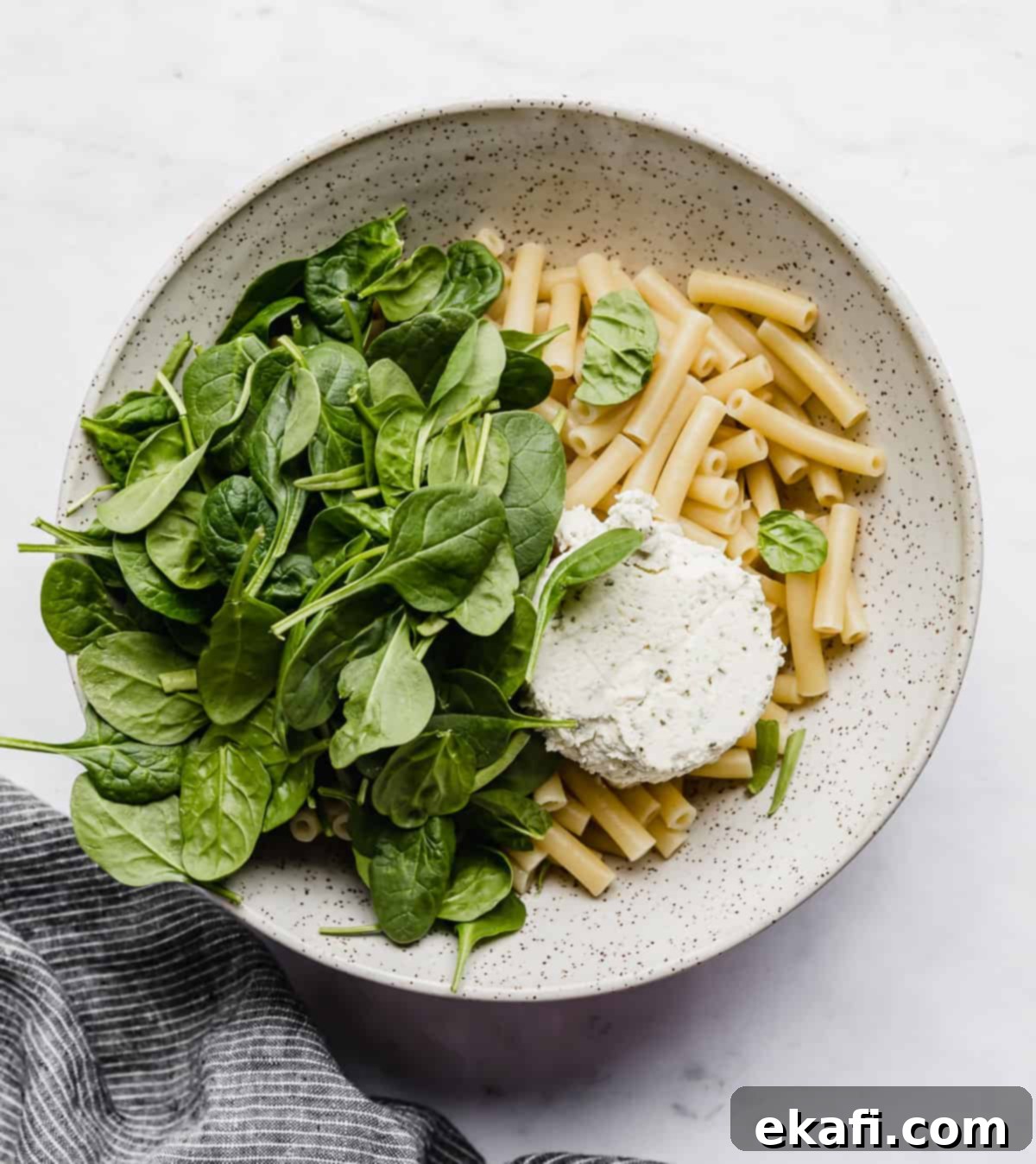 Creamy Boursin Pasta 5 A bowl with cooked pasta noodles, chopped spinach and boursin cheese in it.