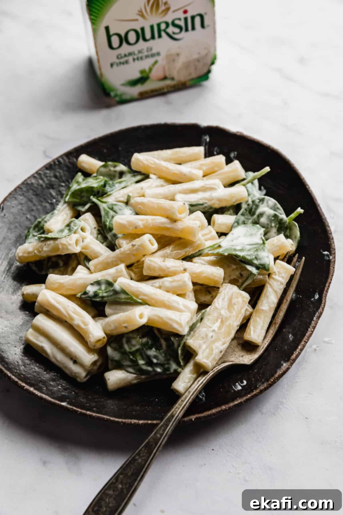 Creamy Boursin Pasta 7 Boursin Pasta with chopped spinach on a black plate with a Boursin white and green cheese box in the background.