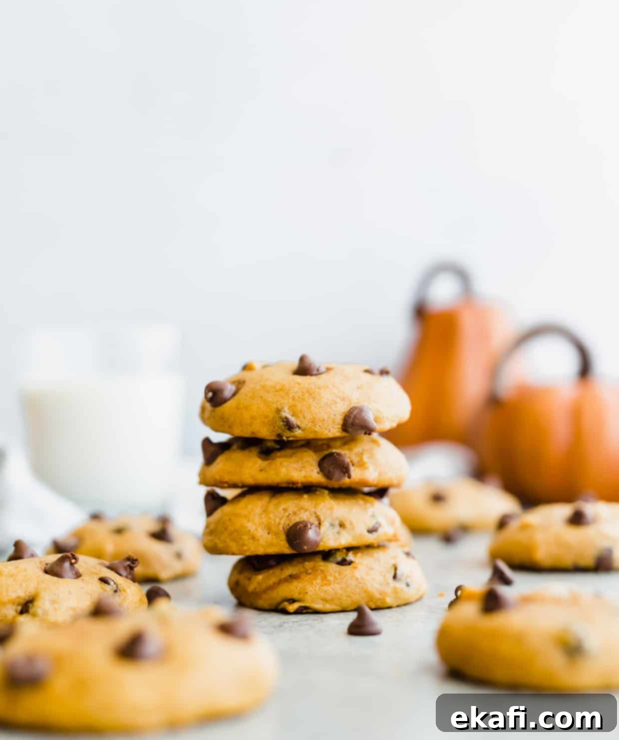 Spiced Pumpkin Chocolate Chip Delights 2 A stack of 4 perfectly baked, soft pumpkin chocolate chip cookies with two decorative pumpkins in the background, evoking a cozy fall feeling.