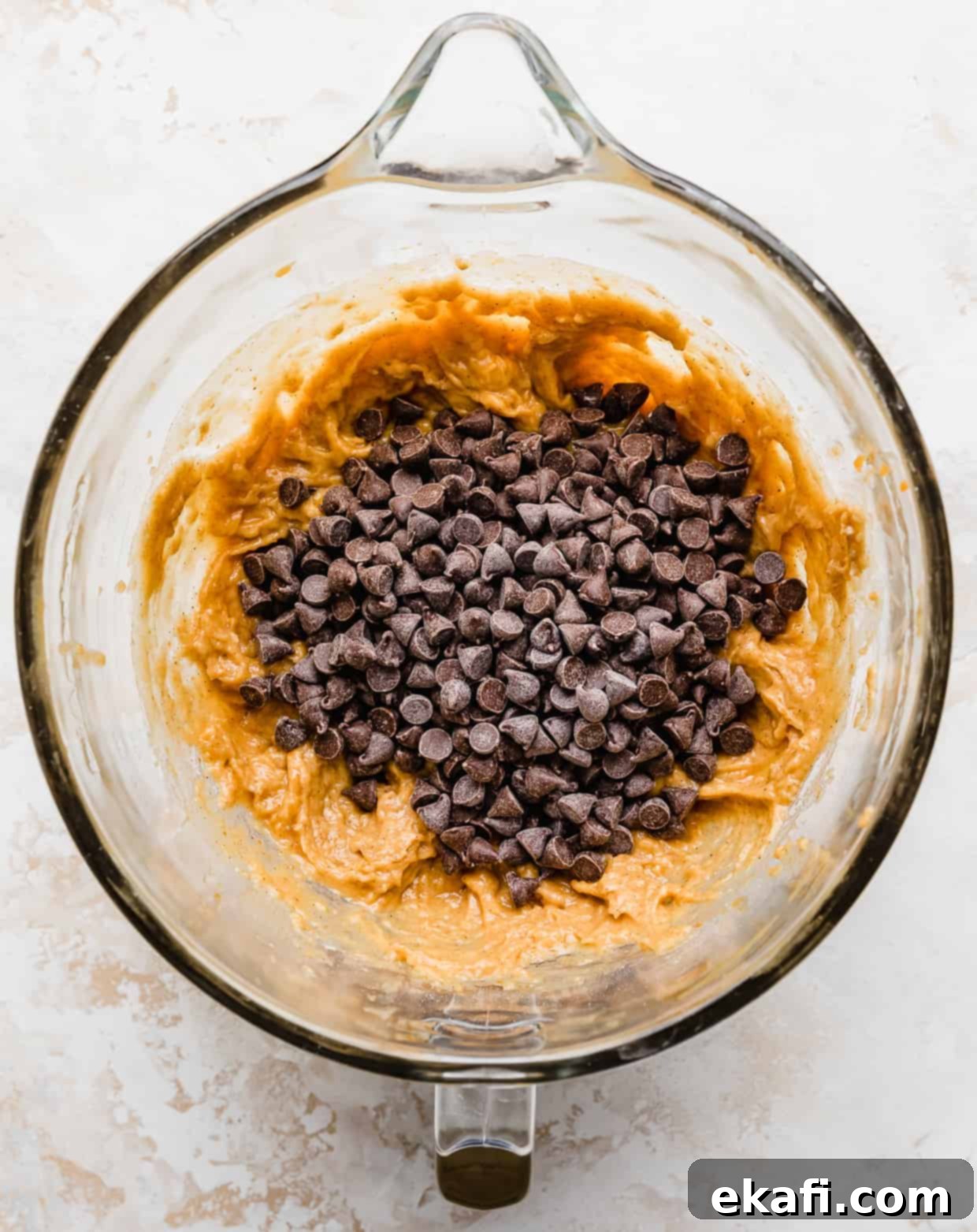 Spiced Pumpkin Chocolate Chip Delights 12 A generous sprinkling of chocolate chips over rich pumpkin chocolate chip cookie dough batter in a glass bowl, ready to be folded in.