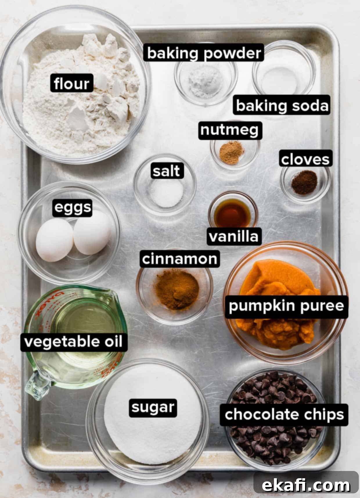 Spiced Pumpkin Chocolate Chip Delights 3 A collection of Pumpkin Chocolate Chip Cookies ingredients, including flour, spices, pumpkin puree, and chocolate chips, neatly arranged on a silver baking sheet.