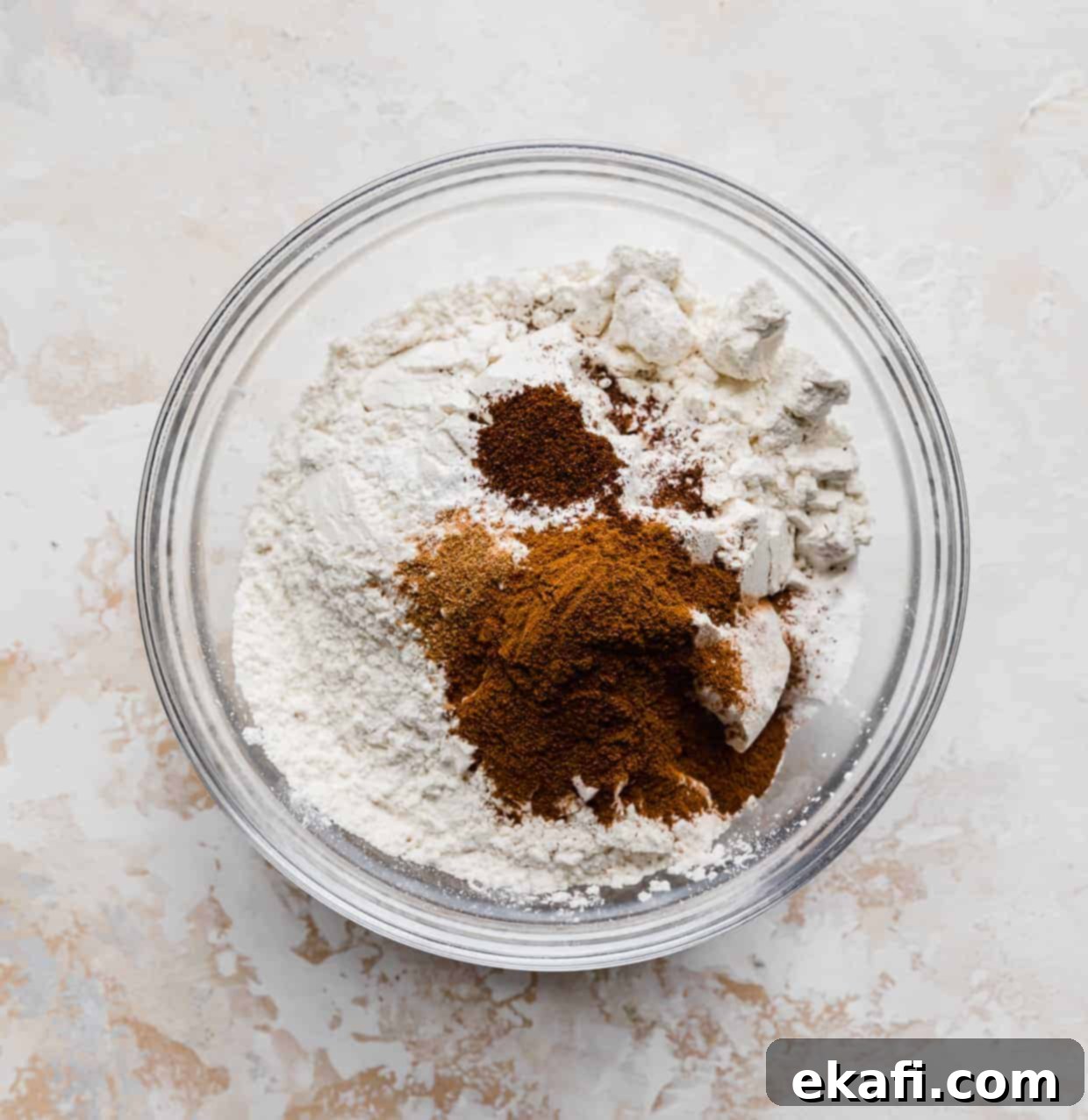 Spiced Pumpkin Chocolate Chip Delights 4 Pumpkin Chocolate Chip Cookie dry ingredients, including flour and spices, carefully measured in a glass bowl on a textured cream background, ready for mixing.