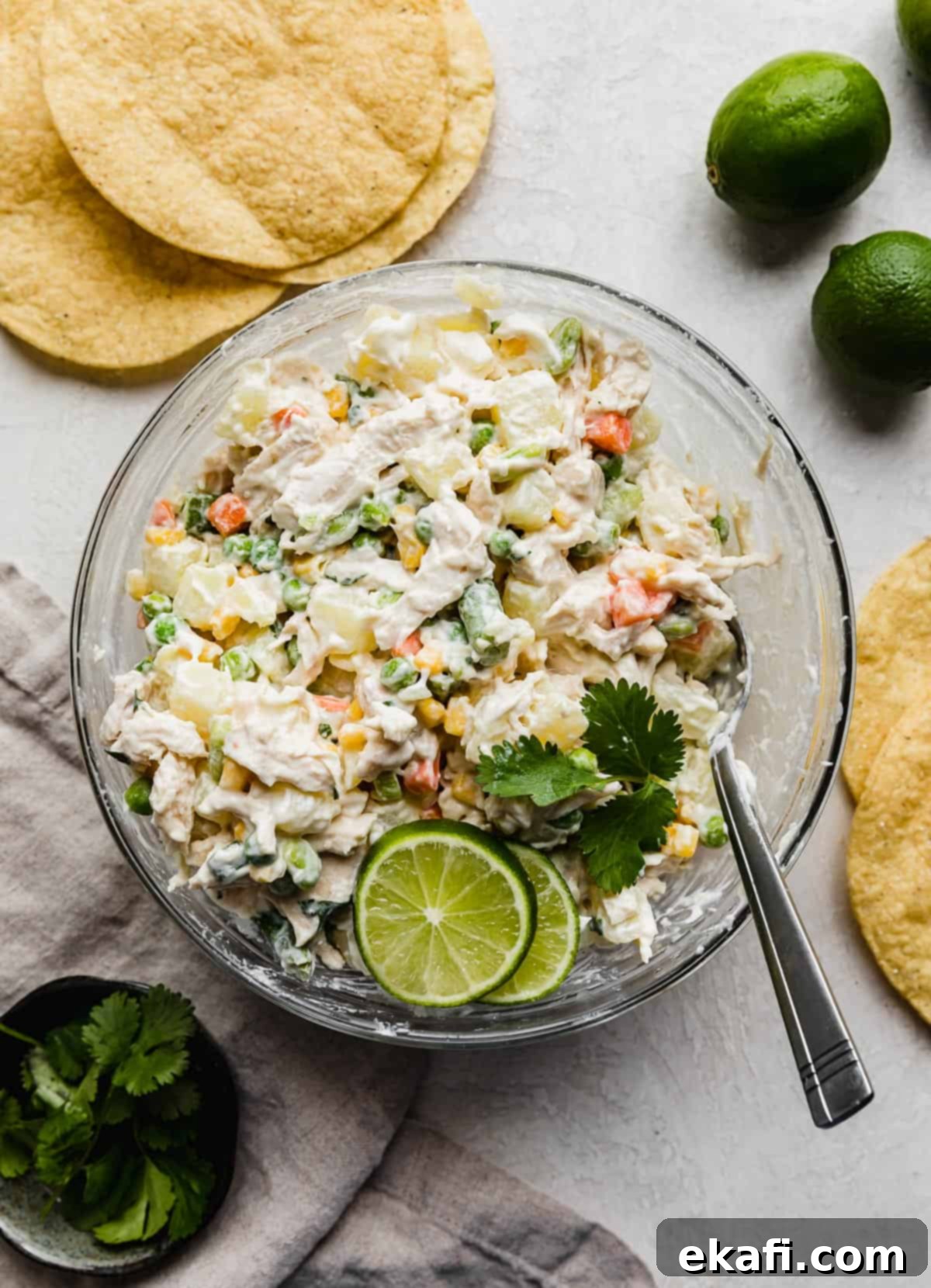 Mexican Chicken Salad 5 Ensalada de pollo in a glass bowl on a light grey background with tostadas and limes beside the bowl.