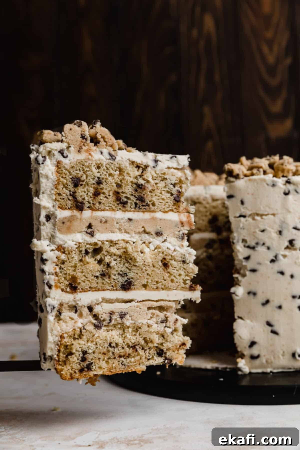 The Ultimate Cookie Dough Dream Cake 11 A tempting slice of layered cookie dough cake on a serving spatula, ready to be enjoyed, against a dark background.