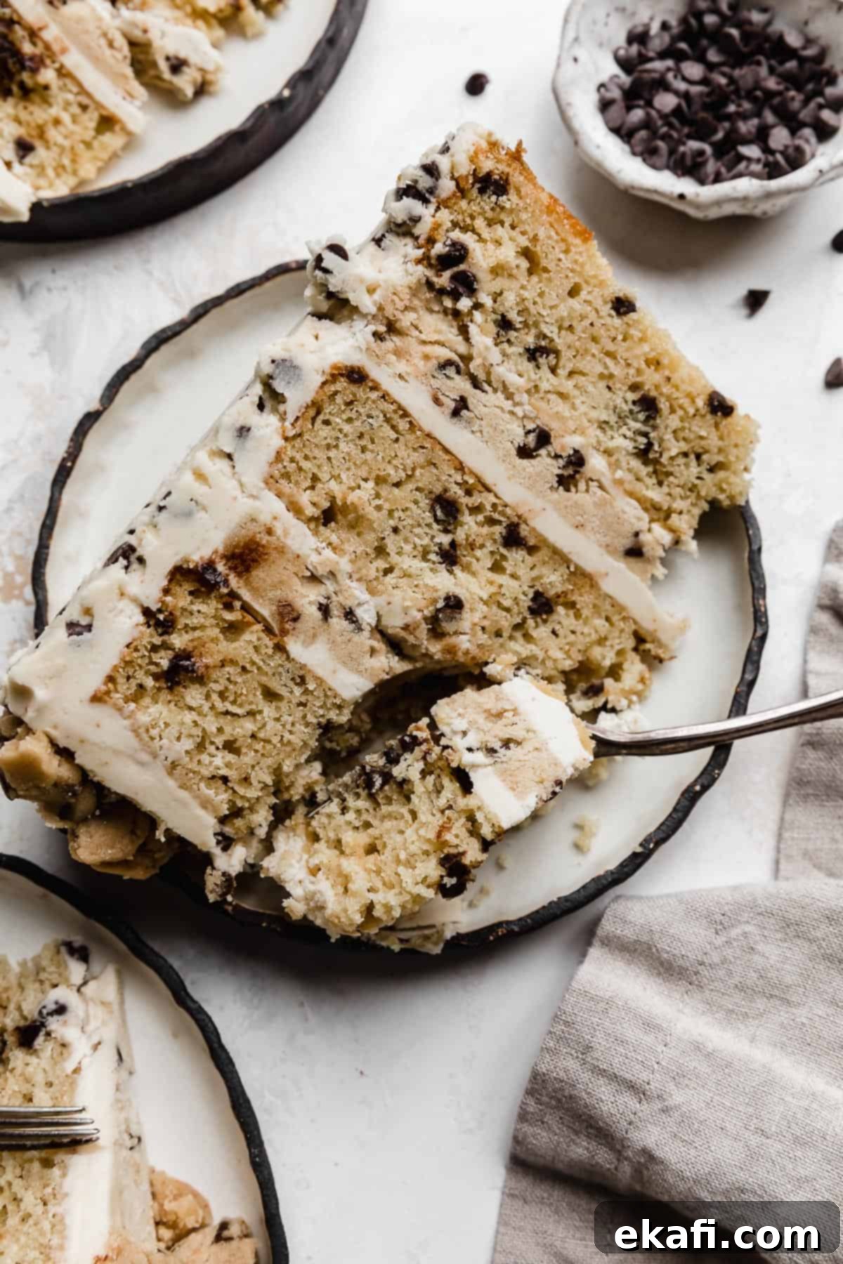 The Ultimate Cookie Dough Dream Cake 13 A delicious slice of Cookie Dough Cake on a black-rimmed white plate, with a fork poised to take a bite.