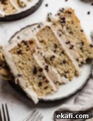 The Ultimate Cookie Dough Dream Cake 14 A three-layer mini chocolate chip Cookie Dough Cake on a white plate against a white background.