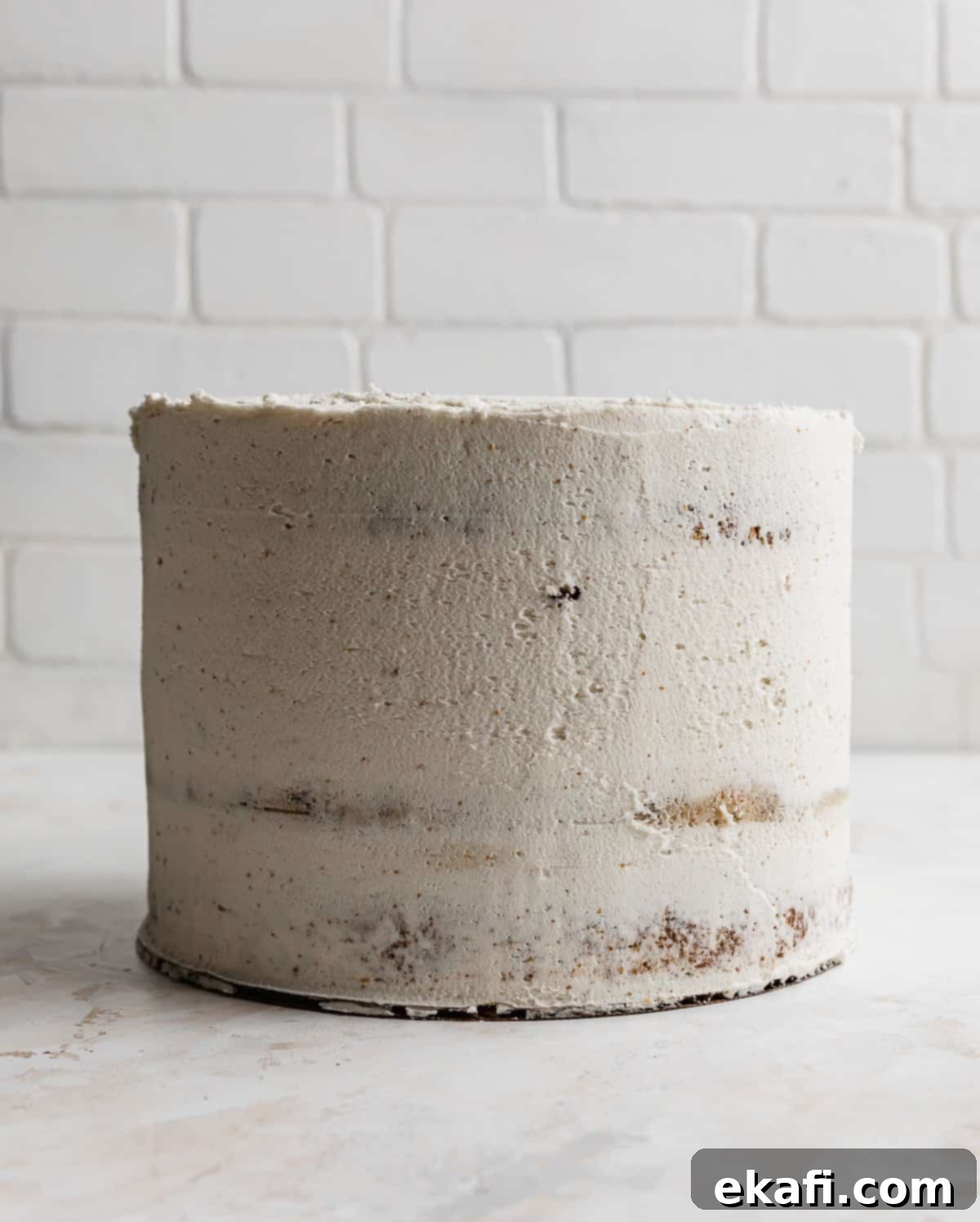 The Ultimate Cookie Dough Dream Cake 8 A three-layer Brown Butter Cookie Dough Cake with a thin crumb coat of white frosting against a white brick background.