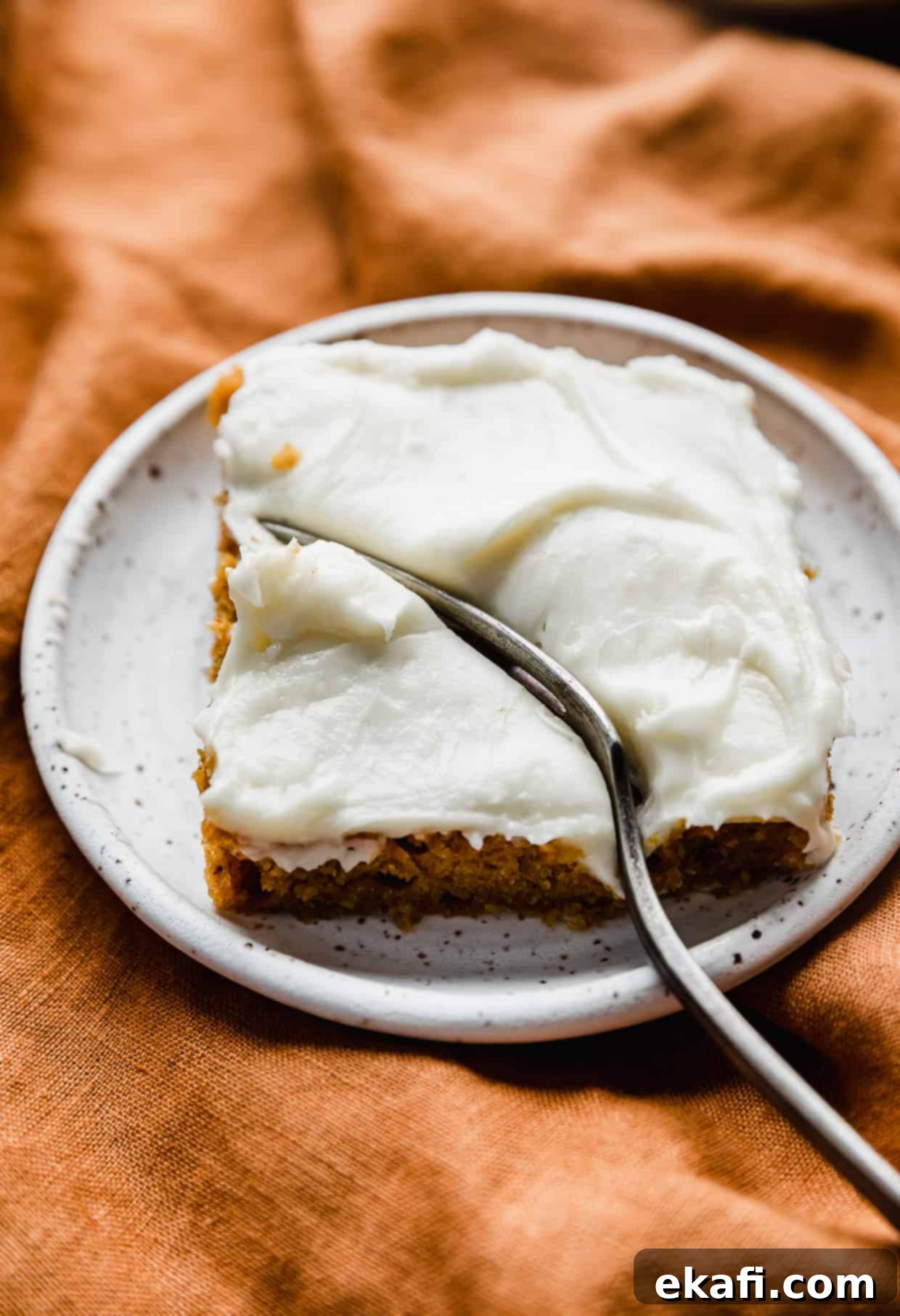 Golden Pumpkin Spice Bars 8 A fork taking a bite out of a square of Libby's Pumpkin Bars with a thick layer of cream cheese frosting.