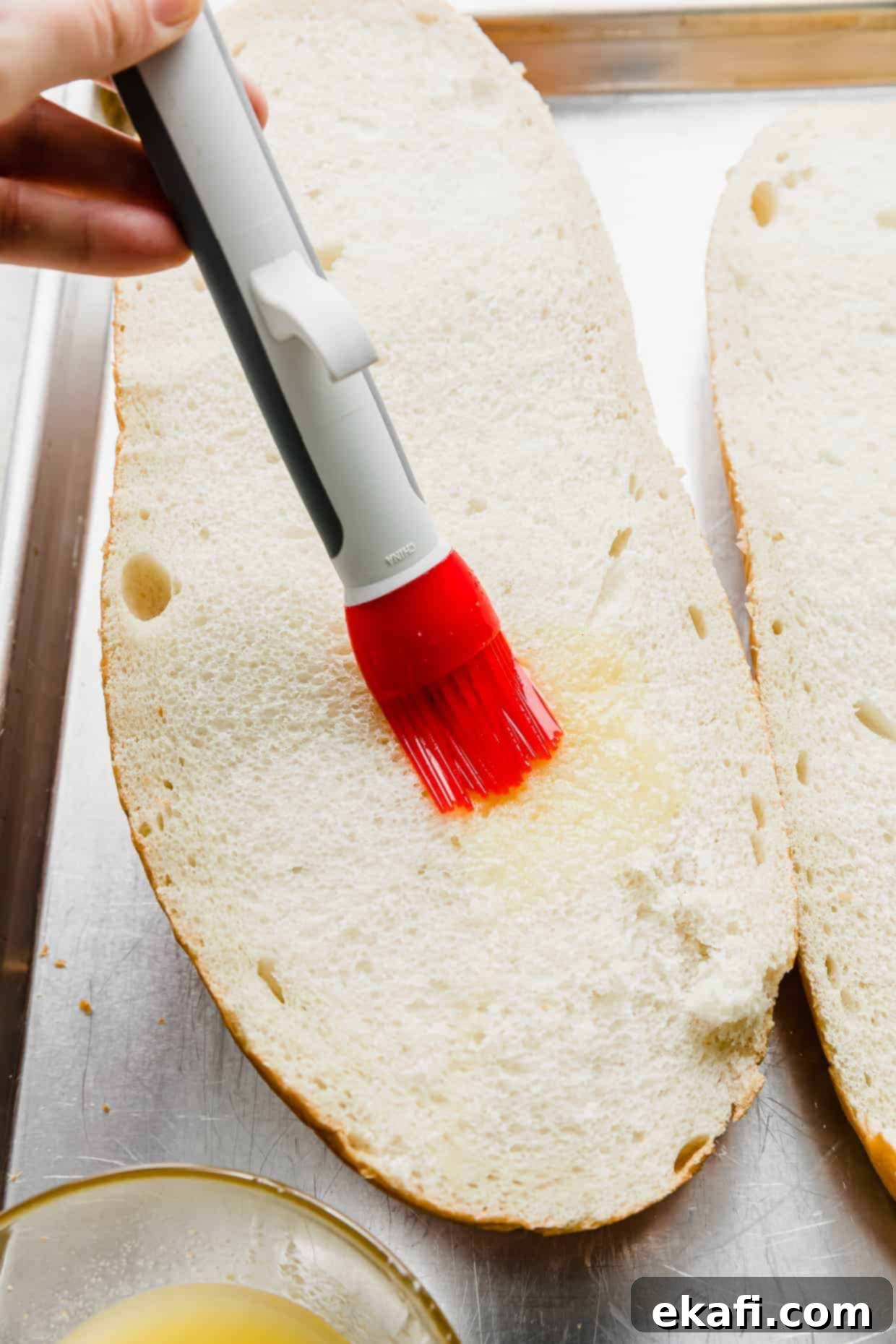 French Bread Pizza 4 A pastry brush spreading melted butter over a slice of French bread.