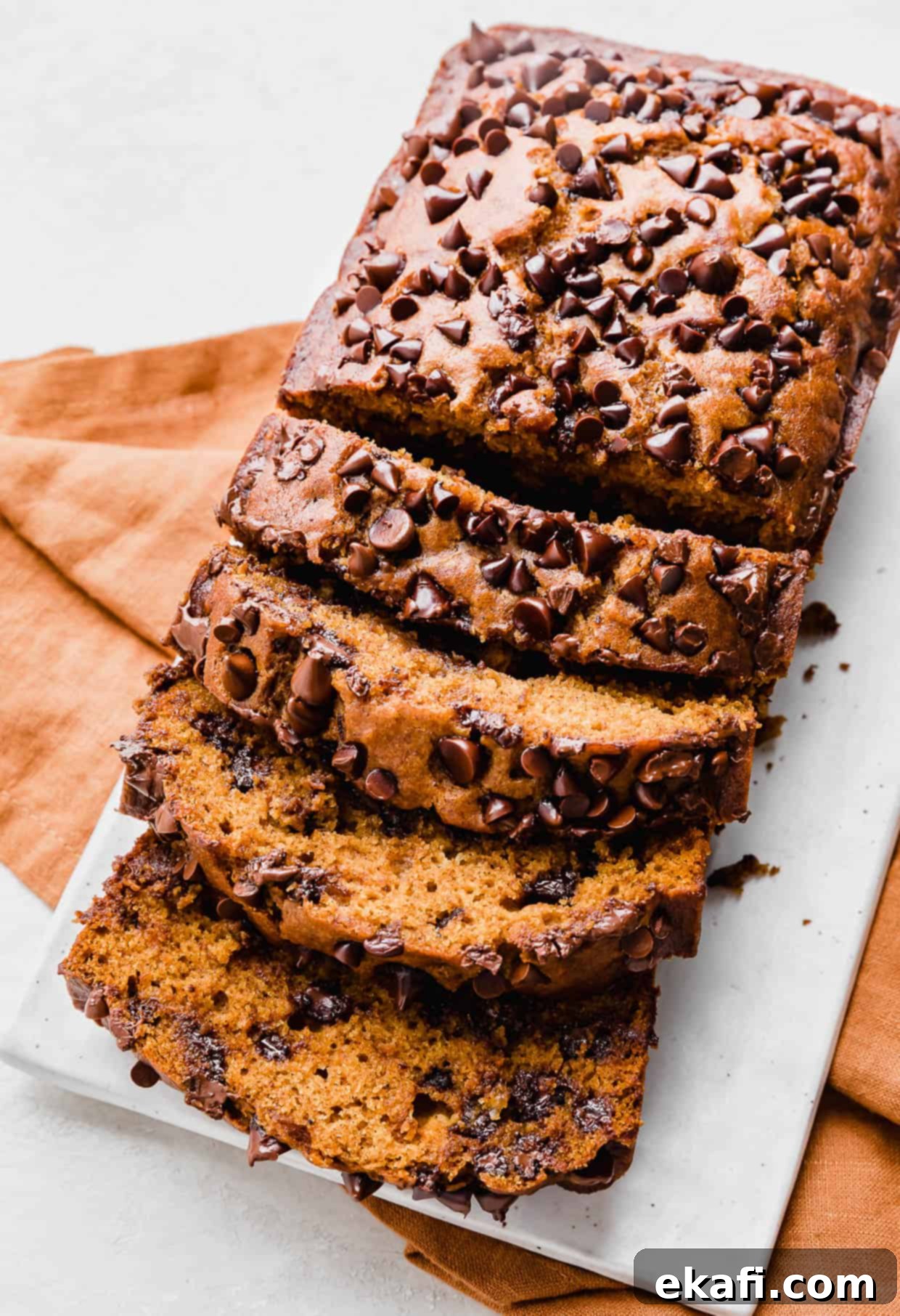 Spiced Chocolate Chip Pumpkin Loaf 2 A sliced Pumpkin Chocolate Chip Bread on a white plate, showing its moist interior and abundance of chocolate chips.