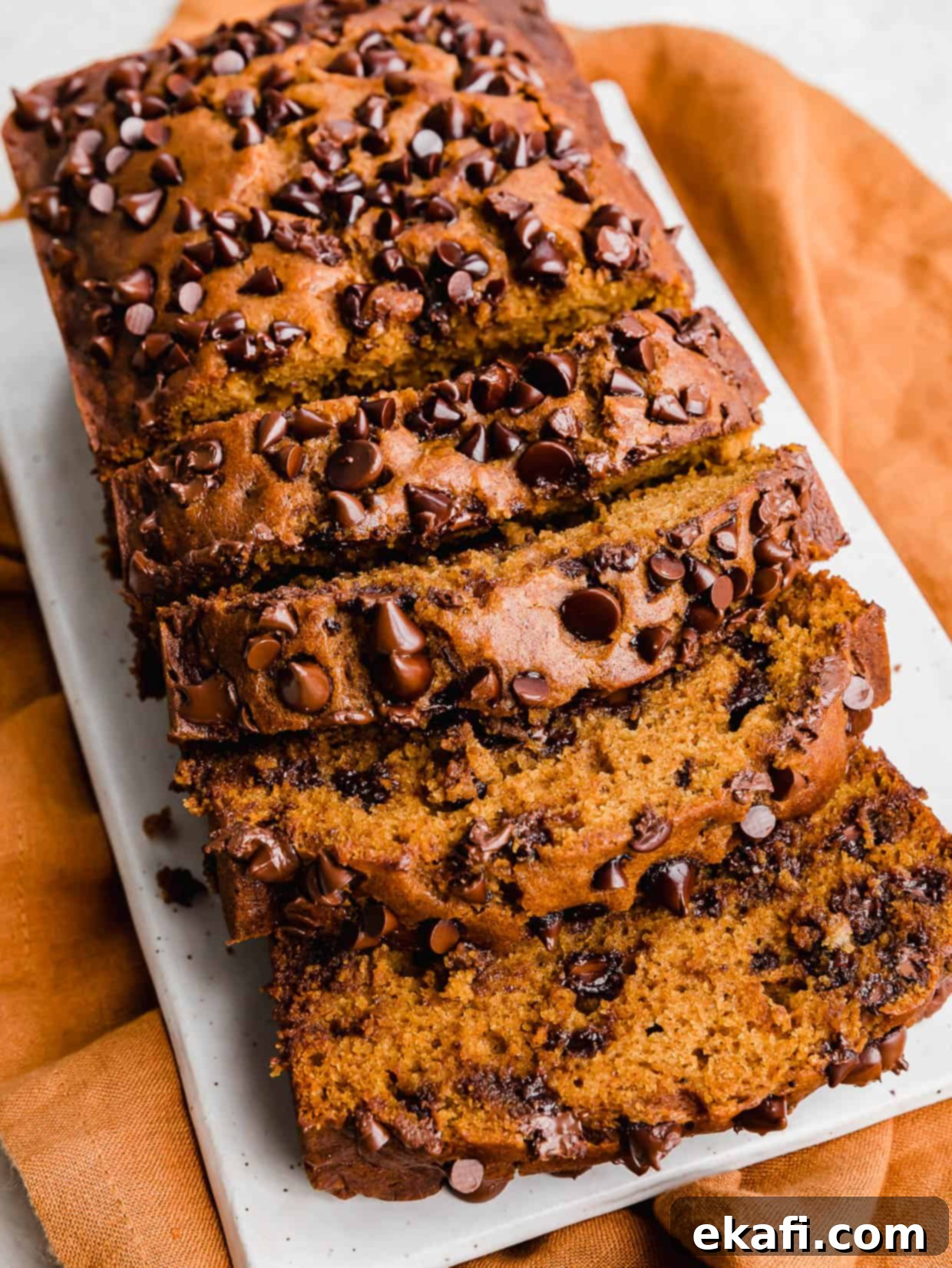 Spiced Chocolate Chip Pumpkin Loaf 8 Pumpkin Chocolate Chip Bread sliced, on a white rectangular plate, showcasing its golden crust and moist interior.