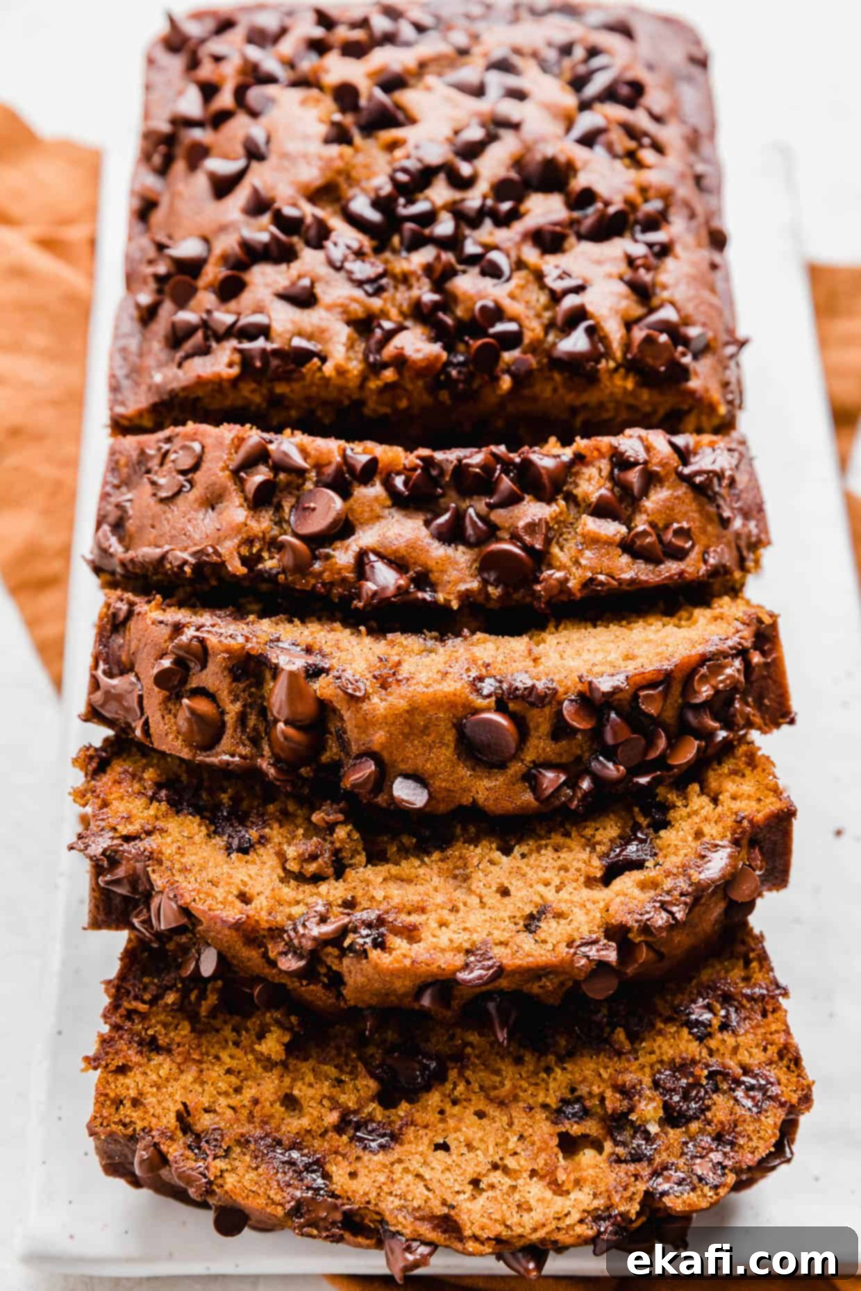 Spiced Chocolate Chip Pumpkin Loaf 9 A whole loaf of Pumpkin Chocolate Chip Bread on a white plate, showcasing its golden crust and delicious appearance.