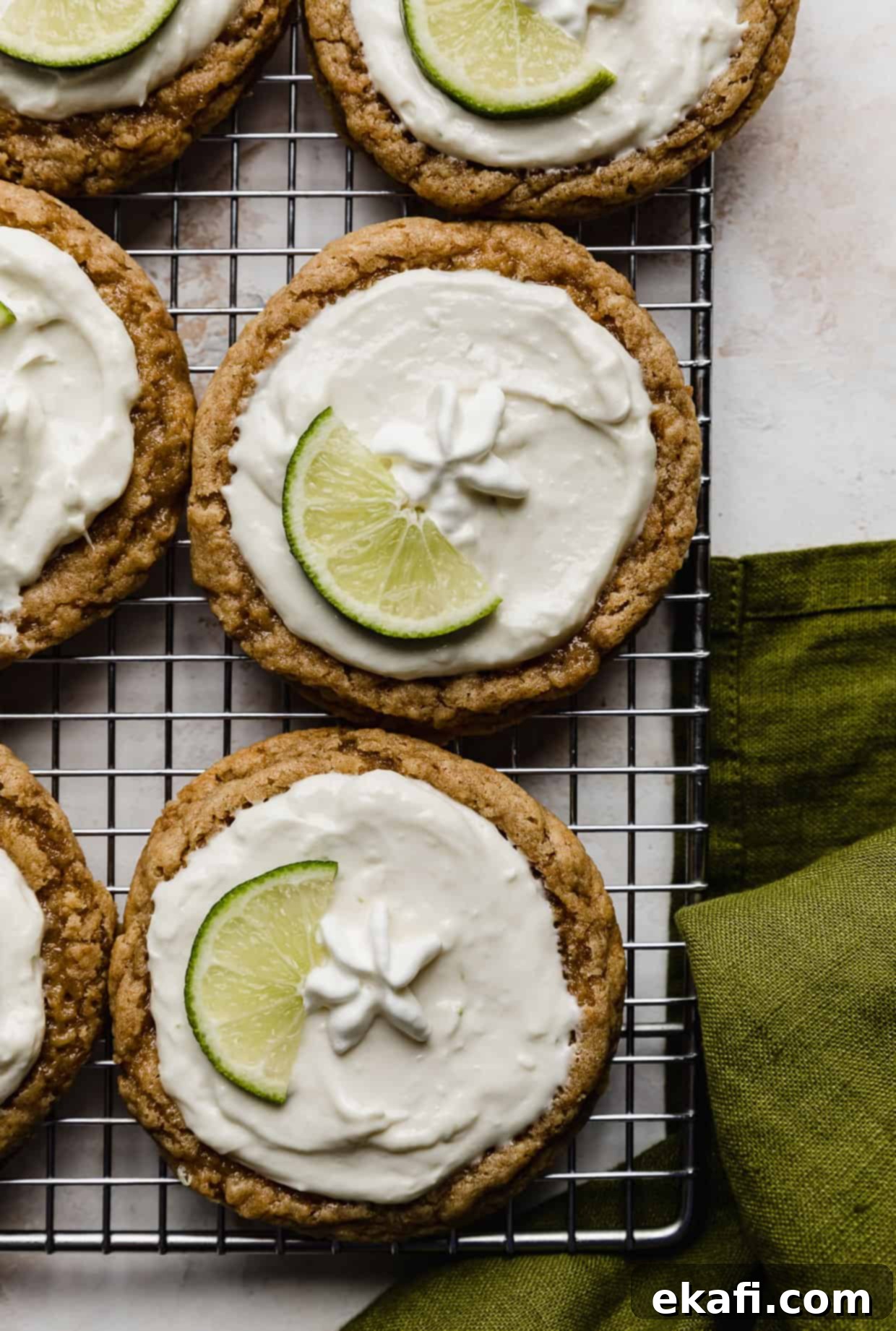 Κράμπλ Μπισκότα Τάρτας Λάιμ 11 Crumbl Key Lime Pie Cookies σε σχάρα ψύξης με πράσινη λινή πετσέτα στην κάτω δεξιά γωνία.