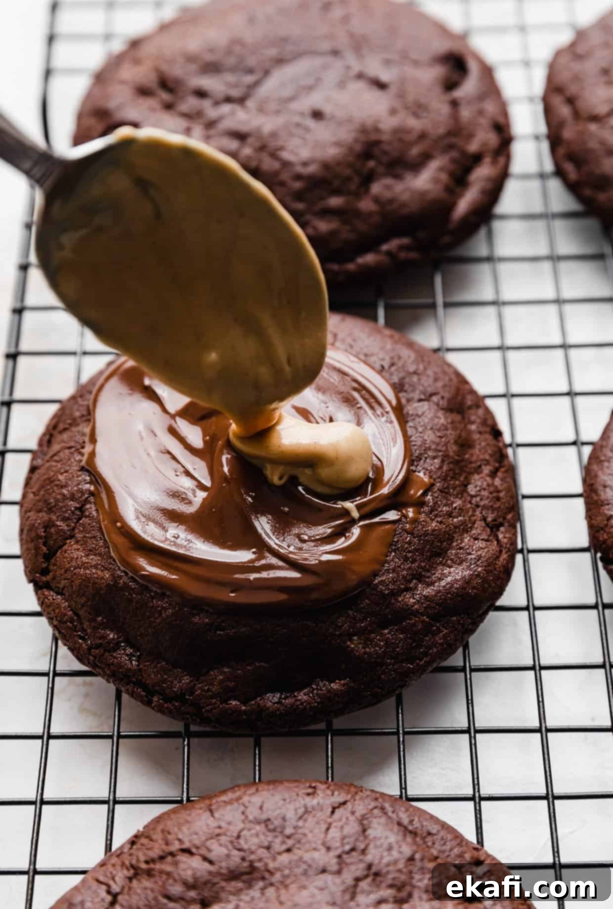 Μπισκότα με φυστικοβούτυρο και καφέ brownie Crumbl 11 Ένα κουτάλι ρίχνει λιωμένο φυστικοβούτυρο πάνω από ένα μπισκότο μπράουνι Crumbl.