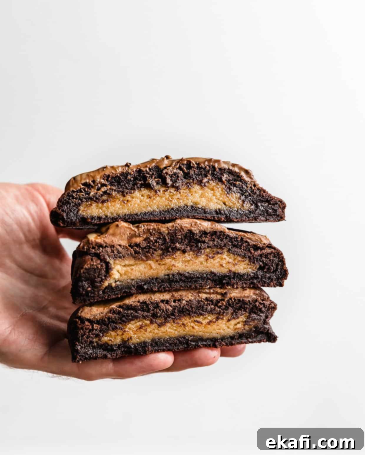 Μπισκότα με φυστικοβούτυρο και καφέ brownie Crumbl 13 Ένα χέρι κρατάει μπισκότα μπράουνι φυστικοβούτυρου σε λευκό φόντο.
