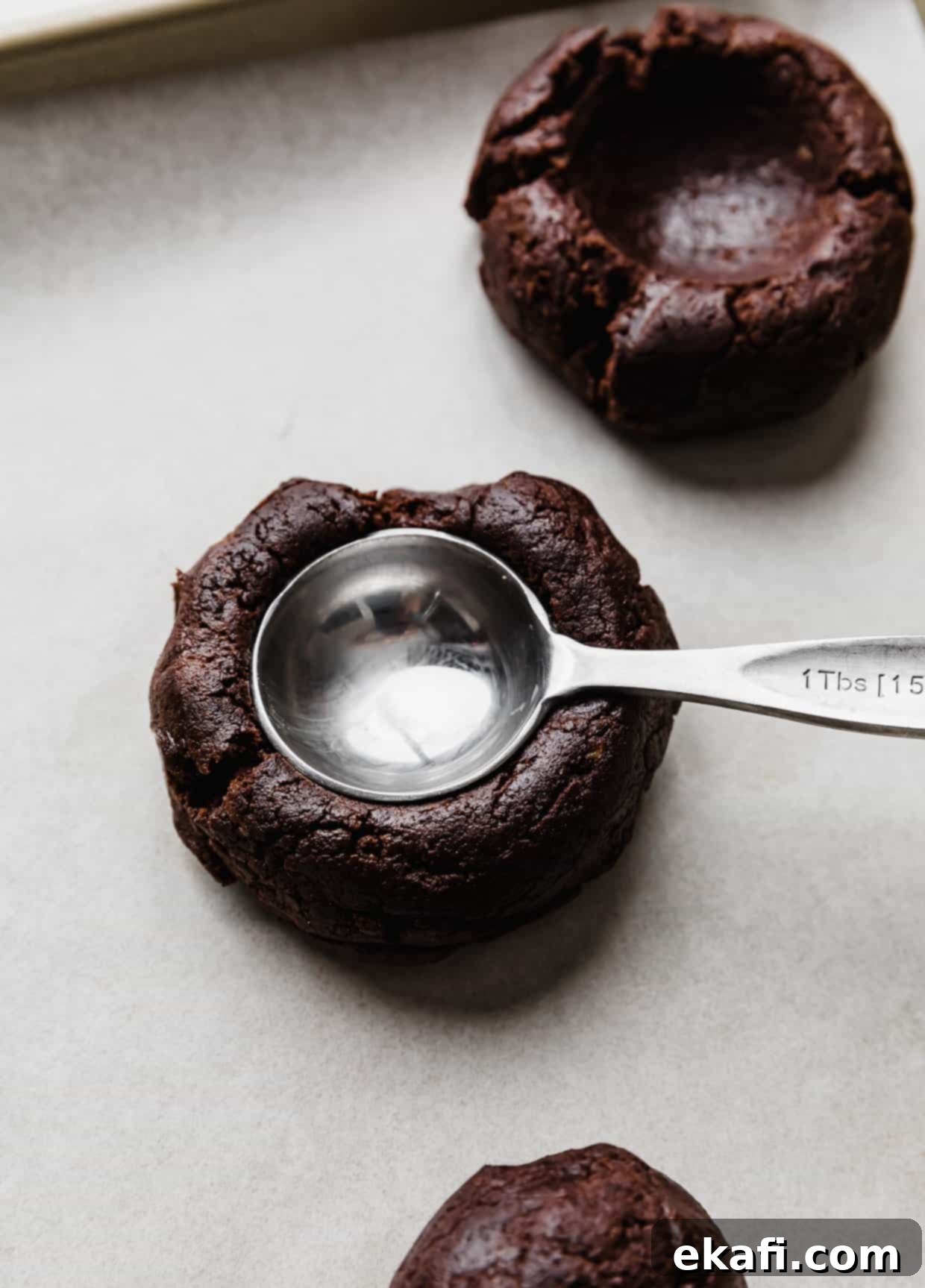 Μπισκότα με φυστικοβούτυρο και καφέ brownie Crumbl 5 Μια καφέ μπάλα ζύμης μπισκότου με μια κουταλιά της σούπας να πιέζει τη ζύμη.