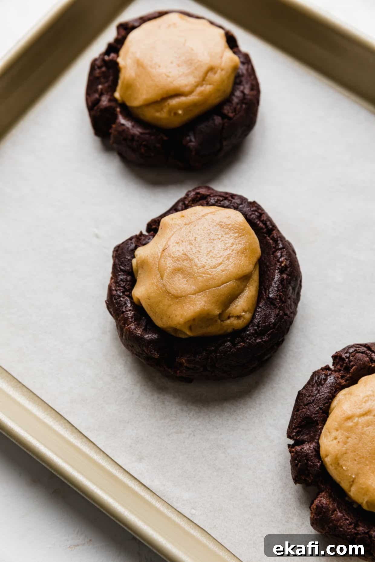 Μπισκότα με φυστικοβούτυρο και καφέ brownie Crumbl 6 Μια μπάλα ζύμης μπισκότου φυστικοβούτυρου πάνω από μια μπάλα ζύμης μπισκότου μπράουνι.