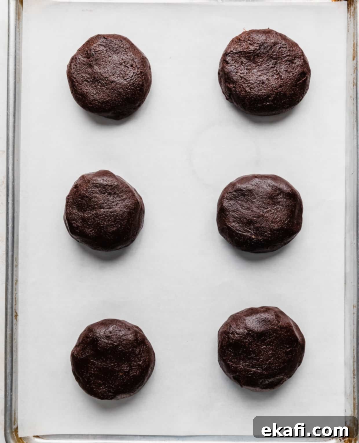 Μπισκότα με φυστικοβούτυρο και καφέ brownie Crumbl 8 Έξι μπάλες ζύμης μπισκότου μπράουνι με φυστικοβούτυρο σε ένα λευκό ταψί καλυμμένο με χαρτί ψησίματος.