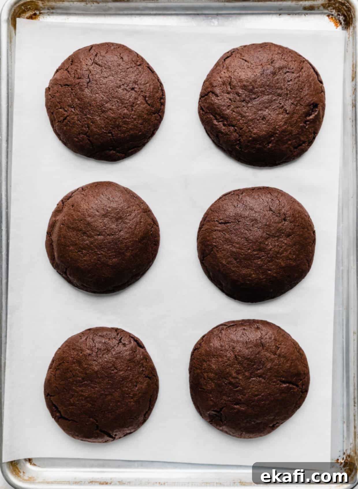 Μπισκότα με φυστικοβούτυρο και καφέ brownie Crumbl 9 Έξι ψημένα μπισκότα μπράουνι σε ένα λευκό χαρτί ψησίματος.