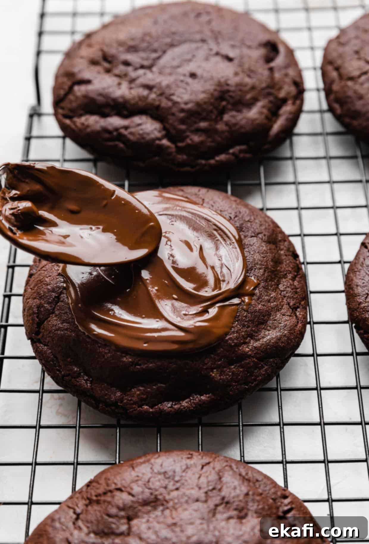 Μπισκότα με φυστικοβούτυρο και καφέ brownie Crumbl 10 Ένα κουτάλι απλώνει λιωμένη σοκολάτα πάνω από ένα μπισκότο μπράουνι φυστικοβούτυρου σε μια σχάρα.