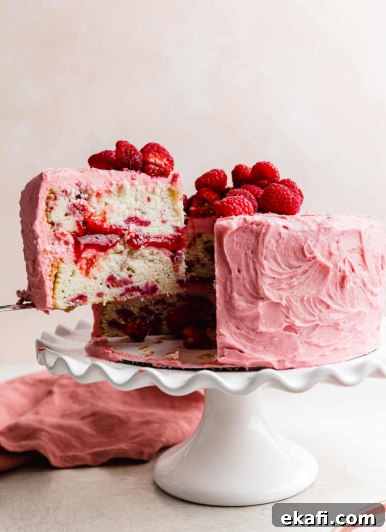 Perfect Lemon Raspberry Cake 2 A slice of fresh Lemon Raspberry layer cake on a knife being lifted from the full cake.